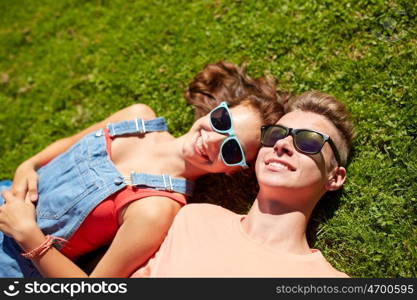 love and people concept - happy teenage couple in sunglasses lying on grass at summer. happy teenage couple lying on grass at summer