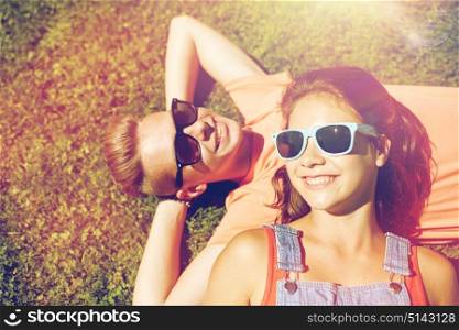love and people concept - happy teenage couple in sunglasses lying on grass at summer. happy teenage couple lying on grass at summer