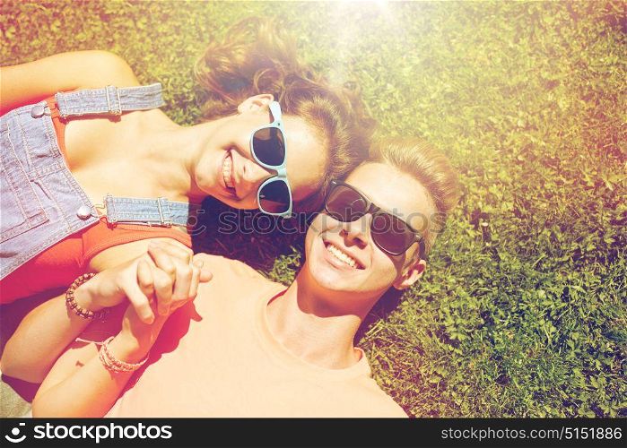 love and people concept - happy teenage couple in sunglasses lying on grass at summer. happy teenage couple lying on grass at summer