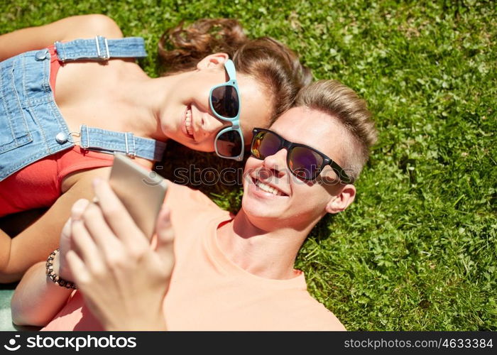 love and people concept - happy teenage couple in sunglasses with smartphone lying on grass at summer. happy teenage couple smartphone lying on grass