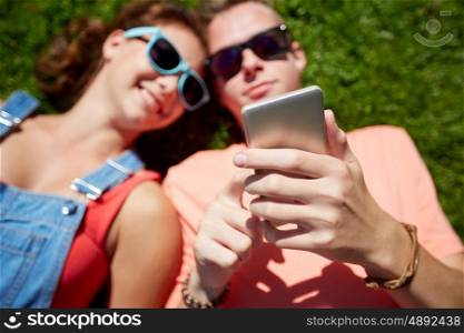 love and people concept - happy teenage couple in sunglasses with smartphone lying on grass at summer. teenage couple with smartphone lying on grass