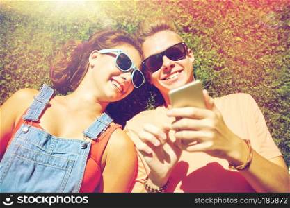 love and people concept - happy teenage couple in sunglasses with smartphone lying on grass at summer. happy teenage couple smartphone lying on grass