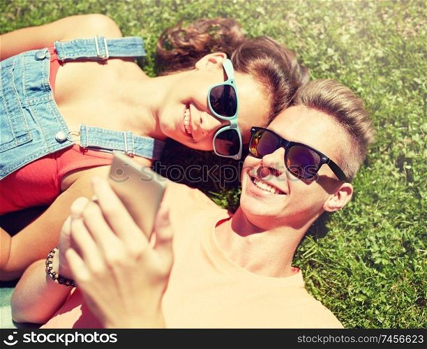 love and people concept - happy teenage couple in sunglasses with smartphone lying on grass at summer. happy teenage couple smartphone lying on grass