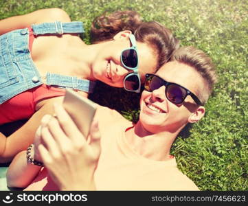 love and people concept - happy teenage couple in sunglasses with smartphone lying on grass at summer. happy teenage couple smartphone lying on grass