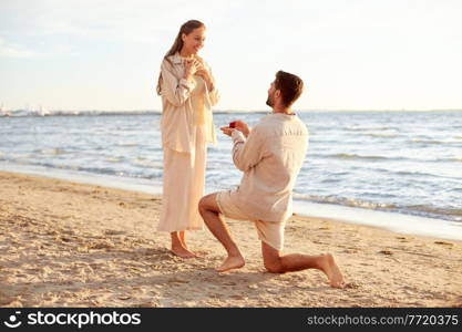 love and people concept - smiling young man with engagement ring making proposal to happy woman on beach. man with ring making proposal to woman on beach