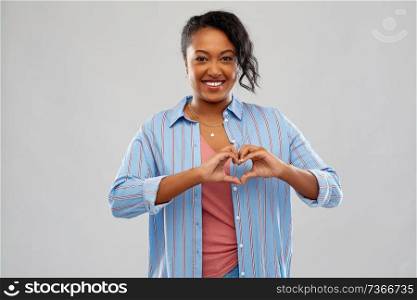 love and valentine&rsquo;s day concept - happy african american young woman making hand heart gesture over grey background. african american woman making hand heart gesture