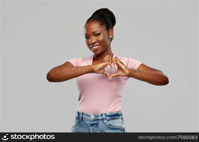 love and valentine&rsquo;s day concept - happy smiling african american young woman making hand heart gesture over grey background. african american woman making hand heart gesture