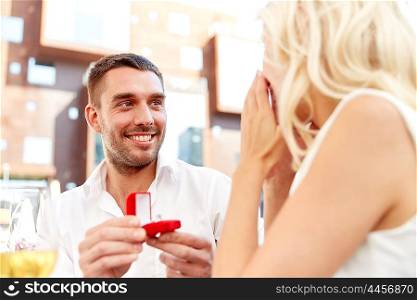 love, anniversary, surprise, people and holidays concept - happy man with engagement ring making proposal to woman at restaurant