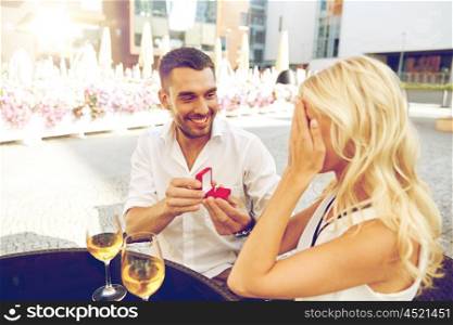 love, anniversary, surprise, people and holidays concept - happy man with engagement ring making proposal to woman at restaurant