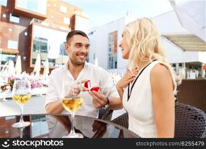love, anniversary, surprise, people and holidays concept - happy man with engagement ring making proposal to woman at restaurant terrace
