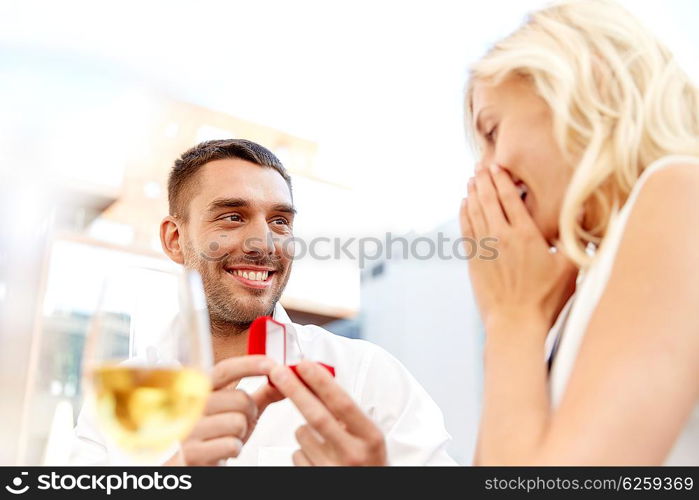 love, anniversary, surprise, people and holidays concept - happy man with engagement ring making proposal to woman at restaurant