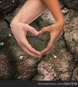 love, care, hope and charity concept - closeup of woman and man hands showing heart shape over ground background