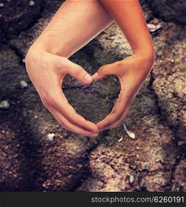love, care, hope and charity concept - closeup of woman and man hands showing heart shape over ground background
