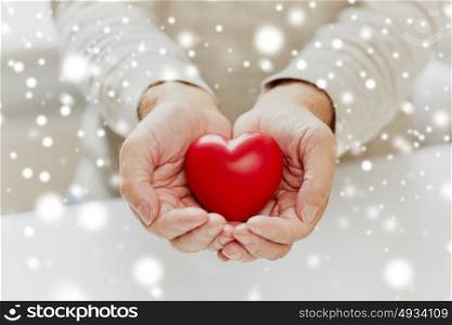 love, charity and people concept - close up of senior man with red heart in hands over snow. close up of senior man with red heart in hands