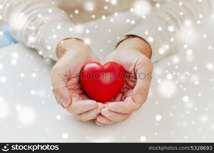 love, charity and people concept - close up of senior man with red heart in hands over snow. close up of senior man with red heart in hands