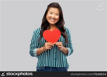 love, charity and valentines day concept - happy asian young woman with red heart over grey background. happy asian woman with red heart