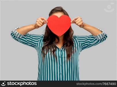 love, charity and valentines day concept - young woman covering her face with red heart over grey background. woman covering her face with red heart