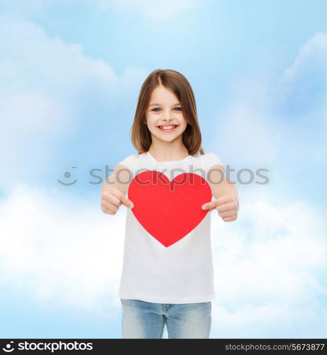 love, charity, childhood and people concept - beautiful little girl sitting at table and holding red heart cutout over cloudy sky background
