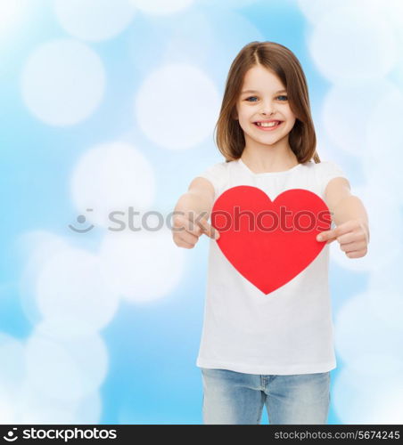 love, charity, childhood and people concept - beautiful little girl sitting at table and holding red heart over blue background