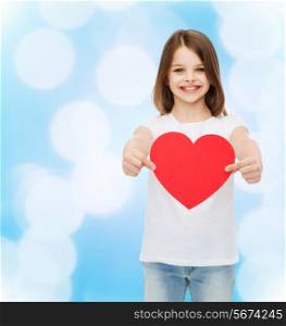 love, charity, childhood and people concept - beautiful little girl sitting at table and holding red heart over blue background