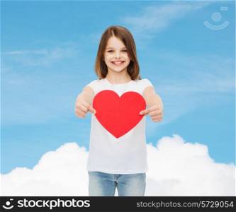 love, charity, childhood and people concept - beautiful little girl sitting at table and holding red heart cutout over blue sky background