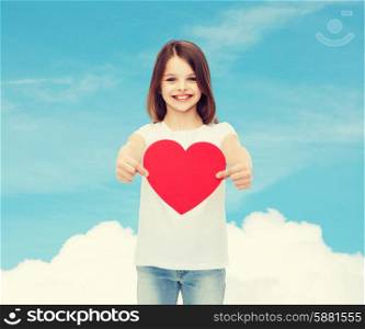 love, charity, childhood and people concept - beautiful little girl sitting at table and holding red heart cutout over blue sky background