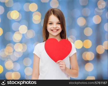 love, charity, holidays, children and people concept - smiling little girl with red heart over blue lights background