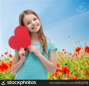 love, charity, holidays, children and people concept - smiling little girl with red heart over blue sky and poppy field background