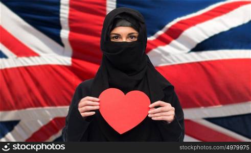 love, charity, immigration, valentines day and people concept - muslim woman in hijab holding red heart over british flag background. muslim woman in hijab holding red heart
