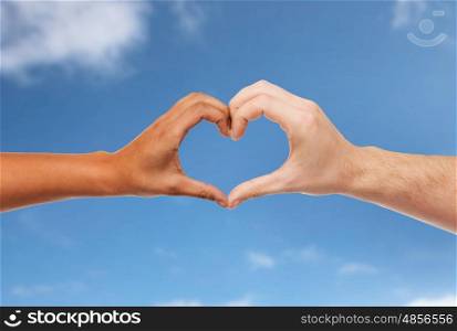 love, charity, valentines day and international concept - close up of man and woman hands making heart symbol over blue sky and clouds background