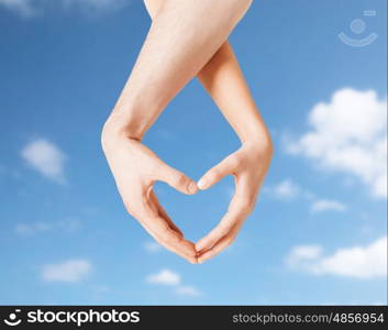 love, charity, valentines day and people concept - close up of man and woman hands making heart symbol over blue sky and clouds background