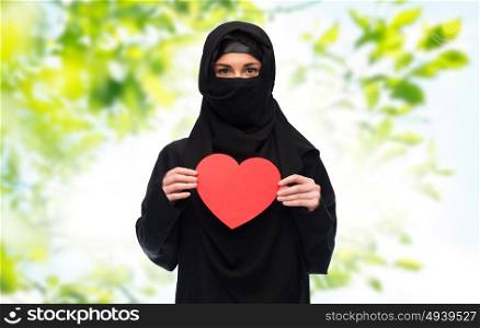 love, charity, valentines day and people concept - muslim woman in hijab holding red heart over green natural background. muslim woman in hijab holding red heart