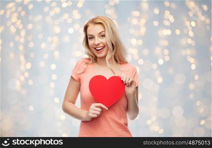 love, charity, valentines day and people concept - smiling young woman or teenage girl with blank red heart shape over holidays lights background