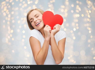 love, charity, valentines day and people concept - smiling young woman or teenage girl with blank red heart shape over holidays lights background