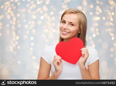 love, charity, valentines day and people concept - smiling young woman or teenage girl with blank red heart shape over holidays lights background