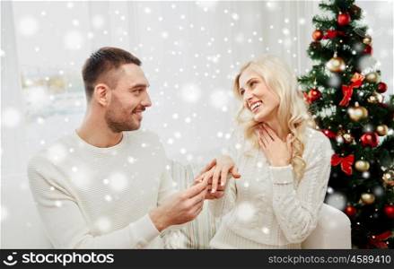 love, christmas, couple, present and people concept - happy man giving engagement diamond ring to woman at home