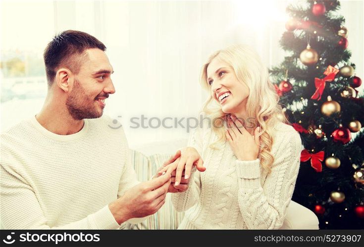 love, christmas, couple, present and people concept - happy man giving engagement diamond ring to woman at home. man giving engagement ring to woman for christmas