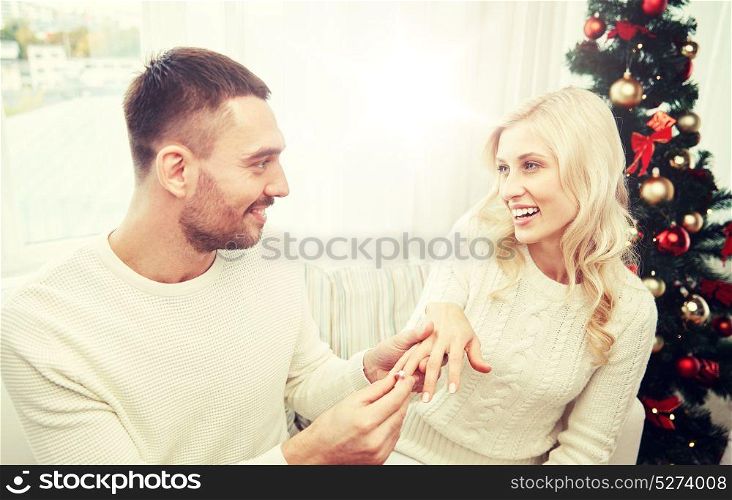 love, christmas, couple, present and people concept - happy man giving engagement diamond ring to woman at home. man giving engagement ring to woman for christmas