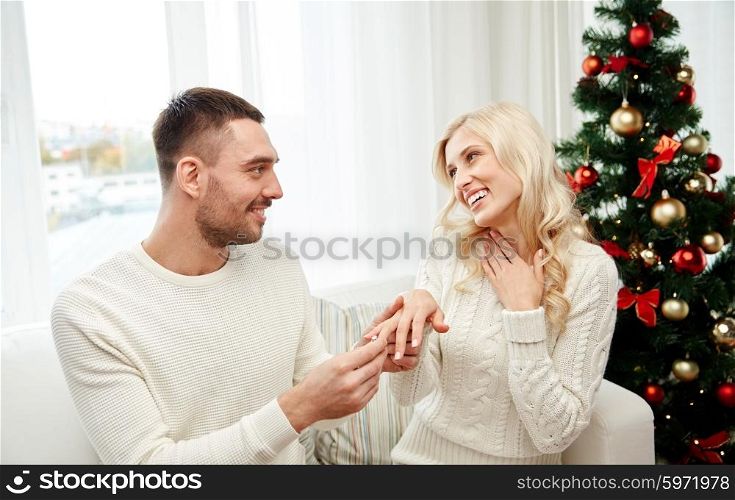 love, christmas, couple, present and people concept - happy man giving engagement diamond ring to woman at home