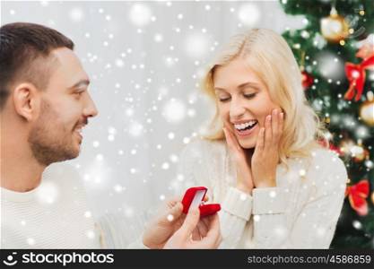 love, christmas, couple, proposal and people concept - happy man giving diamond engagement ring in little red box to woman at home