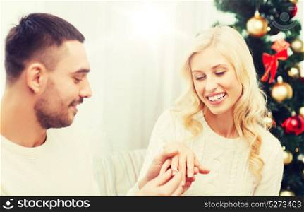 love, christmas, couple, proposal and people concept - happy man giving diamond engagement ring to woman at home. man giving woman engagement ring for christmas