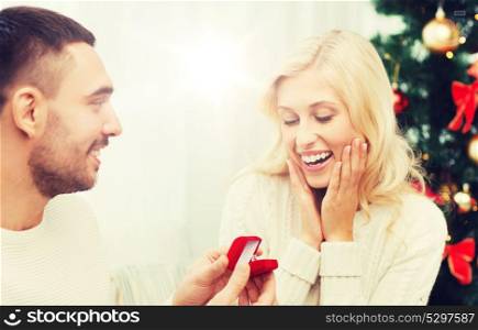 love, christmas, couple, proposal and people concept - happy man giving diamond engagement ring in little red box to woman at home. man giving woman engagement ring for christmas