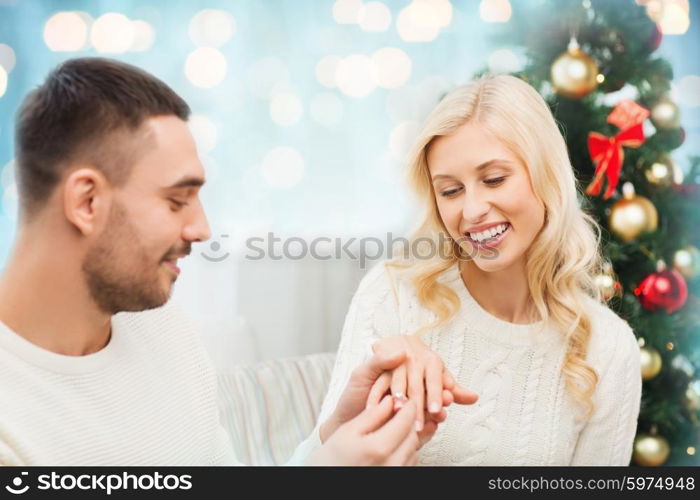 love, christmas, couple, proposal and people concept - happy man giving diamond engagement ring to woman over blue holidays lights background