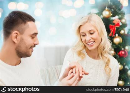 love, christmas, couple, proposal and people concept - happy man giving diamond engagement ring to woman over blue holidays lights background