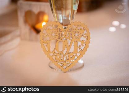 Love concept. Champagne glass with love text and heart shapes on accessories in a wedding setting
