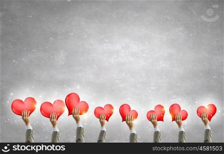 Love concept in hands. Group of people holding heart cards in raised hands