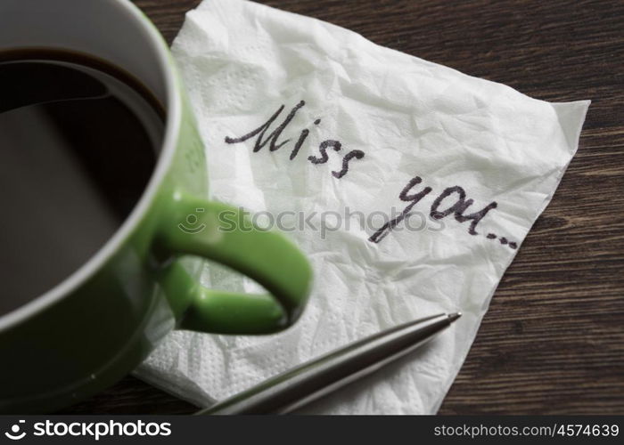 Love confession on napkin. Romantic message written on napkin and cup of coffee on wooden table