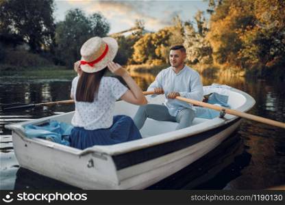 Love couple boating on lake at summer day. Romantic data, boat ride, man and woman walking along the river. Love couple boating on lake at summer day