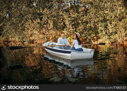 Love couple boating on lake at summer day, water reflection. Romantic data, boat ride, man and woman walking along the river. Love couple boating on lake, water reflection