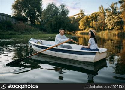Love couple boating on lake at summer day, water reflection. Romantic data, boat ride, man and woman walking along the lake. Love couple boating on lake, water reflection